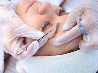 Young woman plucking eyebrows with tweezers close up.